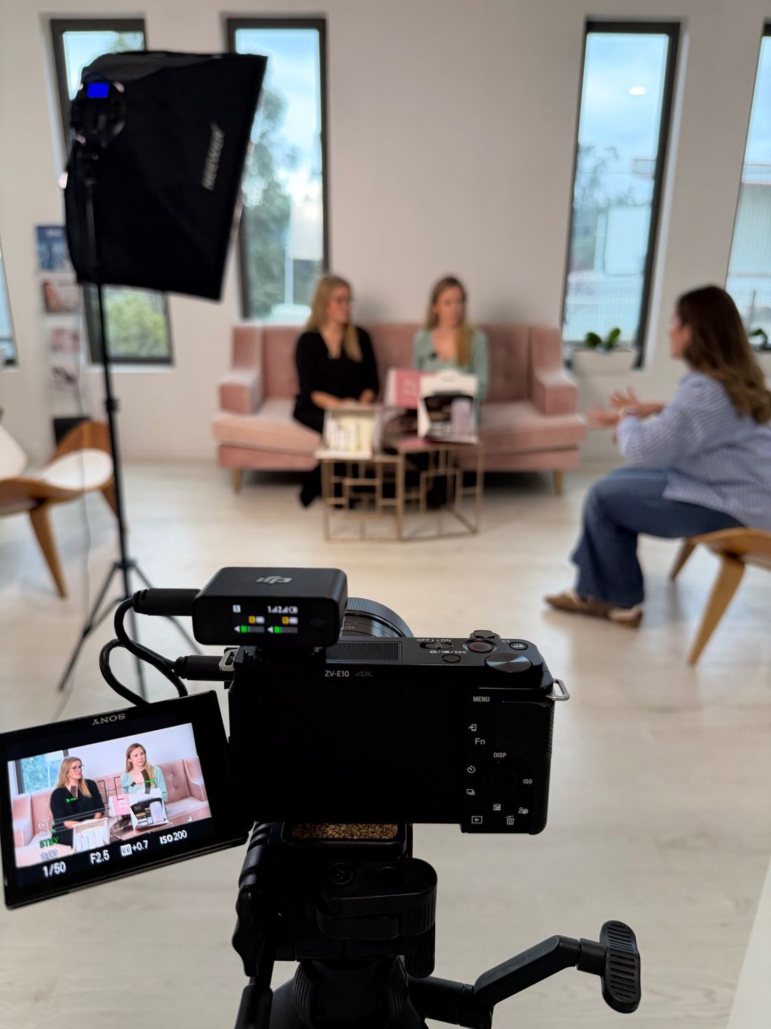 Entrevista a duas convidadas num sofá rosa, vista através da câmara