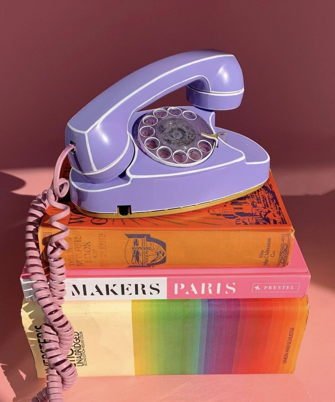 Telefone antigo lilás sobre uma pilha de livros coloridos